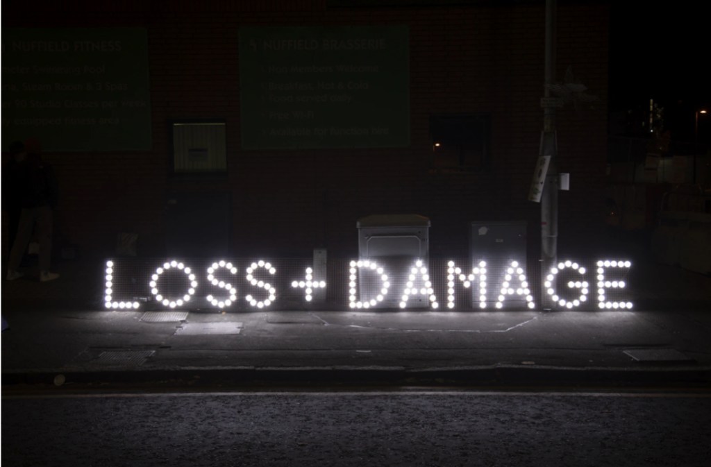 An illuminated sign on a dark urban street reading loss + damage